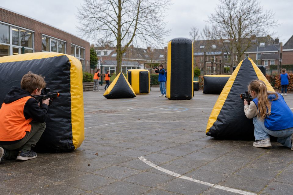 Schoolplein met opblaasbare obstakels en kinderen in oranje en blauwe vesten
